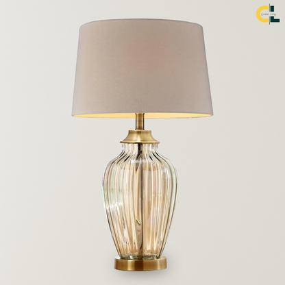 Aquila glass table lamp with a champagne-tinted ribbed base, bronze metal accents, and off-white linen shade, designed for soft ambient lighting on bedside tables, consoles, and living room side tables.