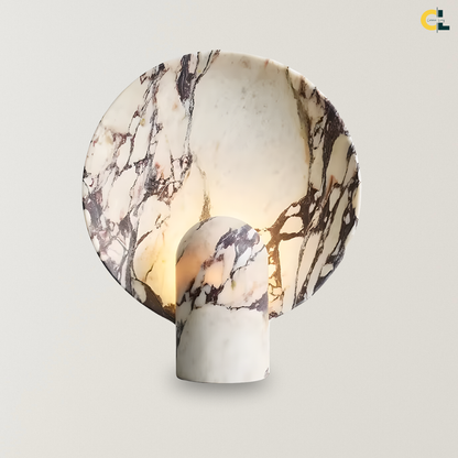 Charity Table Lamp with a sculptural marble and travertine stone form, round veined backplate, and soft warm glow, designed as a refined bedside or console accent lamp.