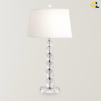 Merlin crystal ball table lamp with a stacked clear glass sphere base and white fabric shade, designed as a refined bedside, desk, console, or living room accent lamp.