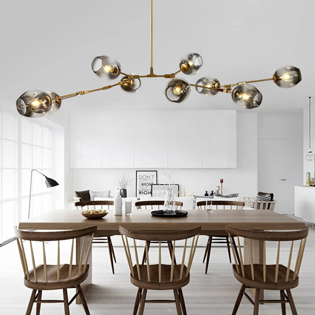 Michaela Glass Chandelier with a gold satellite-style frame, smoky glass globe shades, and warm glowing bulbs suspended above a modern dining table.